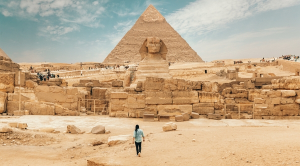 A person walking near the Sphynx and the Pyramids of Egypt.
