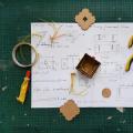 Tools, glue and piece of a prototyped box on a sheet of paper with drawing and dimensions