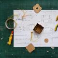 Tools, glue and piece of a prototyped box on a sheet of paper with drawing and dimensions