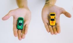 Free Pair of adult hands holding green and yellow toy cars on a white surface, symbolizing choice.